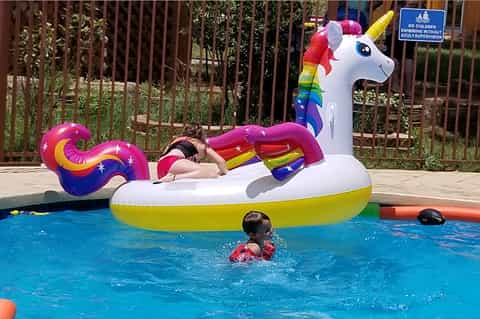 Child on colorful unicorn pool float in bright blue swimming pool with safety fencing