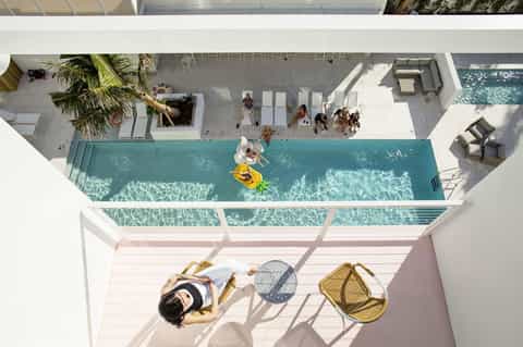 Overhead view of modern resort with rectangular pool, sunbathing guests, and white architecture