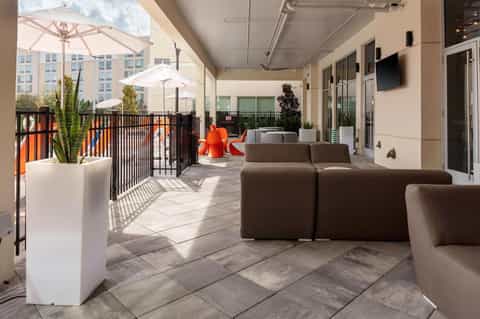 Contemporary rooftop lounge with brown modular seating, white umbrellas, potted plants, and city skyline views