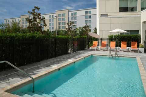 Compact residential pool with turquoise water, orange lounge chairs, and hedge privacy fencing