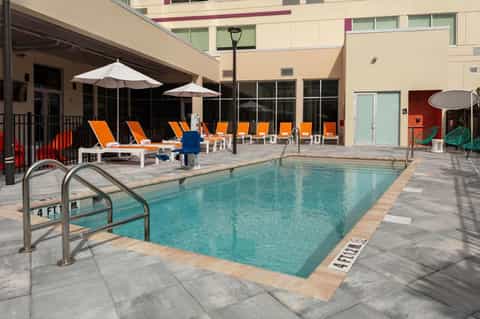 Outdoor pool area with orange lounge chairs, white umbrellas, and modern building at resort