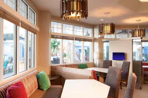 Modern resort lounge with striped seating, wooden pendant lights, ocean view windows, and TV display
