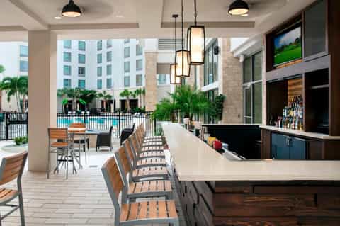 Outdoor poolside bar and lounge with modern seating, palm trees, and contemporary architecture