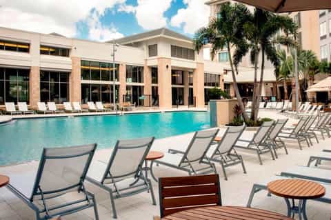 Resort pool with lounge chairs, palm trees, and modern building with brick accents