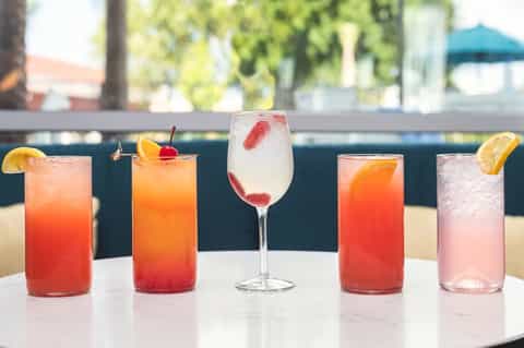 Colorful tropical cocktails lined up on a white counter with citrus garnishes
