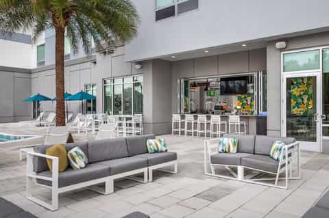 Modern courtyard with lounge seating, blue umbrellas, palm tree, tiki bar, and fireplace seating area