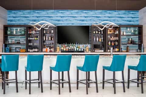 Contemporary bar with turquoise bar stools, blue wave tile backdrop, and illuminated shelving with liquor bottles