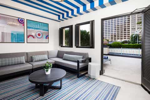 Modern lounge area with striped ceiling, gray seating, blue accent rug, and balcony access