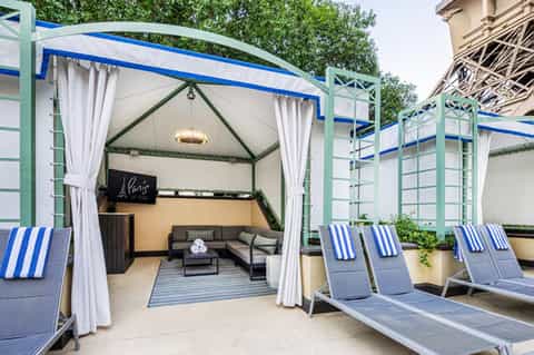 Luxurious cabana with white curtains, blue striped loungers, and seating area