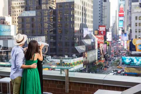 Couple viewing cityscape from observation deck with telescope overlooking Times Square