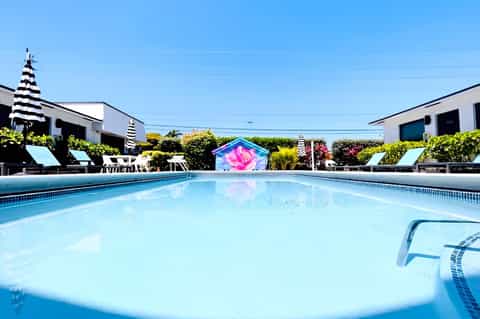 Bright turquoise swimming pool with colorful art installation, palm trees, and modern resort buildings