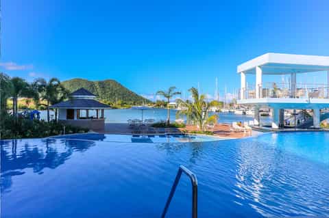 Resort infinity pool overlooking marina with sailboats and palm trees under clear blue sky