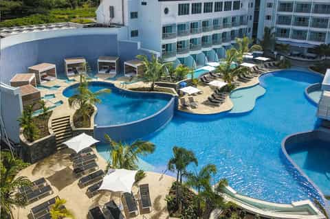 Aerial view of curved resort pools, cabanas, palm trees, and multi-story hotel building