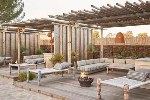 Outdoor patio with wooden pergola, striped cushioned seating, fire pit, and stone wall backdrop