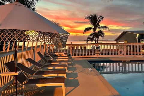 Sunset view of poolside lounge area with palm trees, covered cabana, and waterfront dock