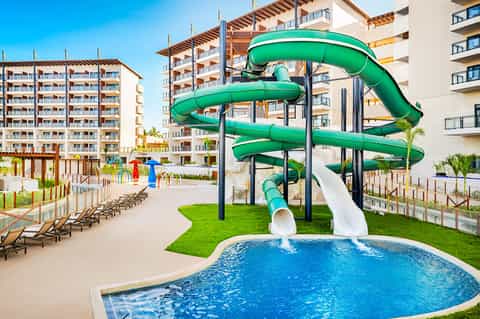 Resort water park with green spiral slide over blue pool, loungers, and multi-story apartment buildings