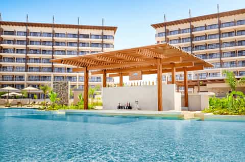 Modern resort pool with wooden pergola structure and tall apartment buildings in the background