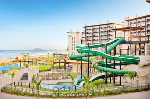 Beachfront resort with green water slides, multi-story residential buildings, sandy beach, and ocean views