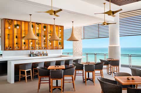 Beachfront bar with orange cabinetry, woven pendant lights, ocean views, and modern seating