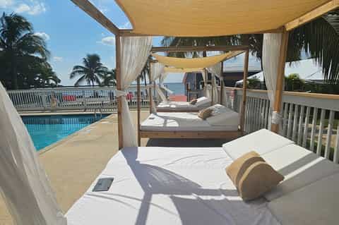 Shaded daybed with ocean view, draped fabric canopy, and adjacent swimming pool