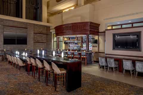 Grand bar lounge with dark wood bar, seating, high ceiling, and ambient lighting