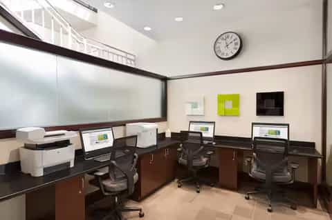 Modern office workspace with dark wood desks, computer monitors, and mesh office chairs