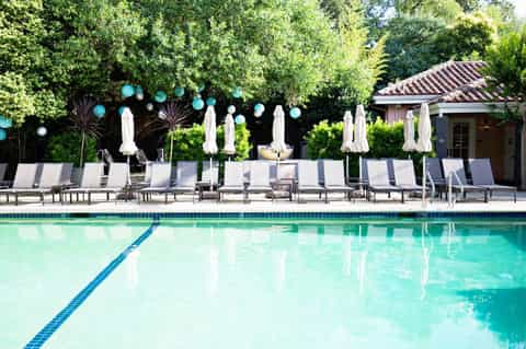 Swimming pool with white umbrellas and lounge chairs surrounded by lush landscaping and decorative lighting