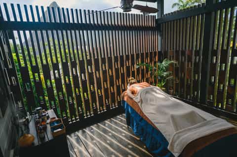 Person relaxing on bed in private balcony with modern slatted railing and tropical greenery