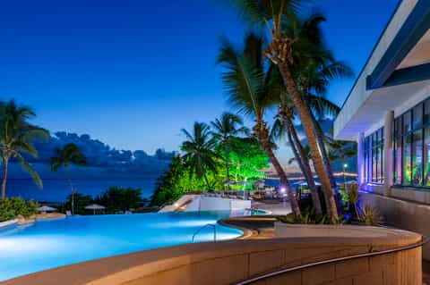 Luxury oceanfront resort with illuminated infinity pool, palm trees, and modern architecture at twilight