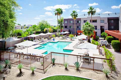 Resort courtyard with turquoise swimming pool, lounge chairs, umbrellas, and modern pink building