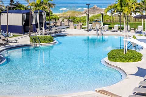 Resort pool complex with blue water, lounge chairs, covered pavilions, and ocean view