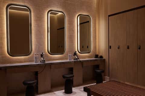 Modern spa bathroom with three illuminated mirrors, wooden vanity, and private changing area with lockers