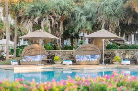 Luxury pool area with two oversized daybed pods, umbrellas, palm trees, and tropical garden setting