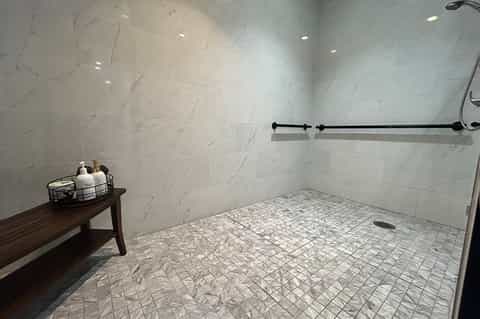 Modern bathroom with marble tile walls, mosaic floor, black towel bar, and amenities basket