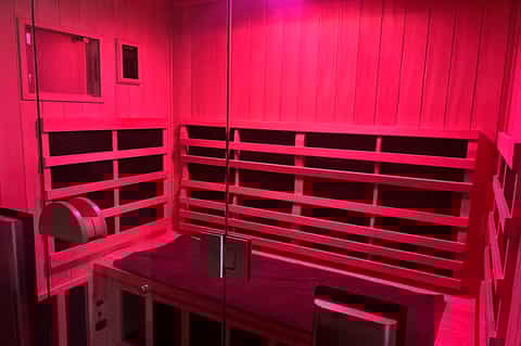 Interior of bright pink infrared sauna with wooden benches and glass door