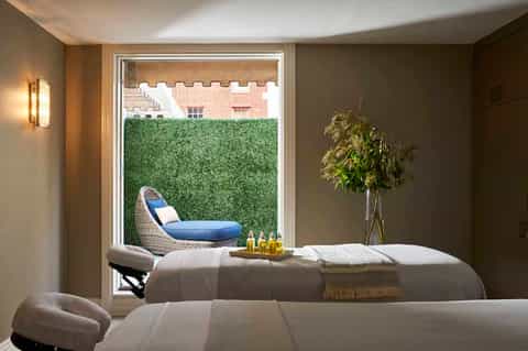 Spa treatment room with massage beds overlooking a garden courtyard and brick building exterior