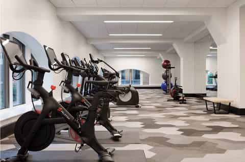 Bright fitness center with row of stationary bikes, exercise equipment, and geometric floor pattern