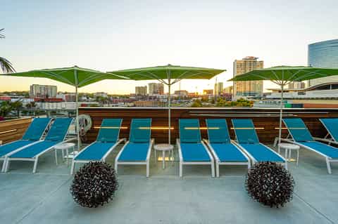 Rooftop deck with blue loungers, green umbrellas, and city skyline at dusk