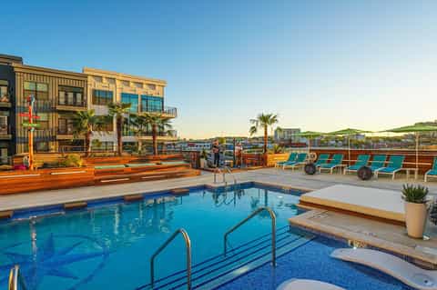 Rooftop pool with city views, colorful lounge chairs, modern buildings, and wooden deck area