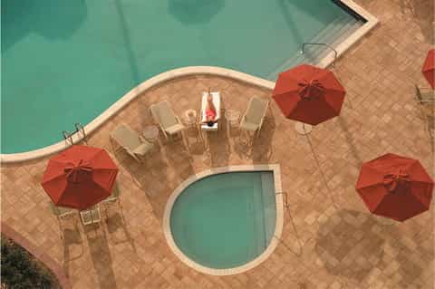 Overhead view of small pool with lounge chairs and red umbrellas on tiled deck with person floating
