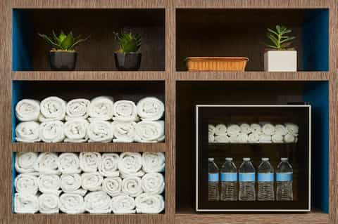 Spa storage shelving with rolled white towels, potted plants, and bottled water