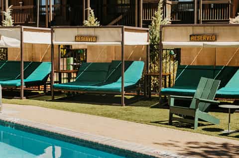 Reserved cabana lounge chairs with turquoise cushions and shade canopies beside an outdoor pool