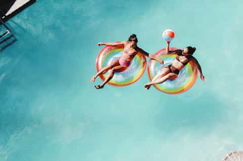 Aerial view of two people floating on colorful rainbow pool floats in bright turquoise water