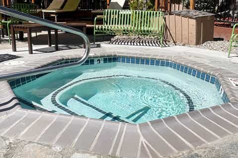 Hot tub surrounded by lounge chairs and green accents on a sunny outdoor deck