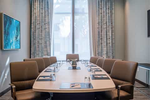Conference room with long table, leather chairs, and large windows with blue artwork on wall