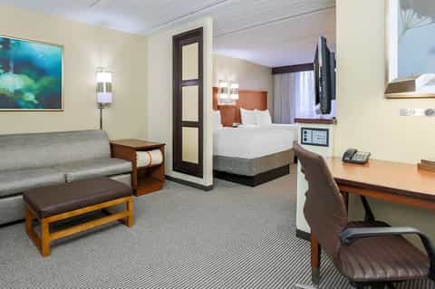 Modern hotel suite with queen bed, sofa, desk workspace, and contemporary furnishings