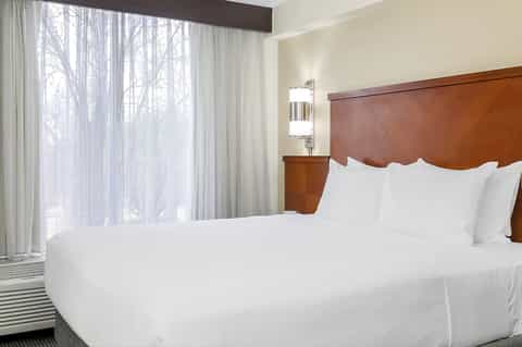 Hotel bedroom with queen bed, wood headboard, large windows overlooking bare winter trees
