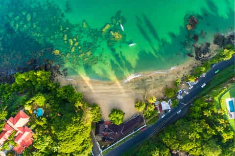 Aerial view of pristine beach cove surrounded by lush green forest with turquoise water