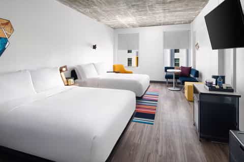 Modern hotel room with two queen beds, white bedding, flat-screen TV, and minimalist décor