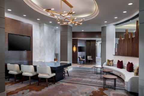 Luxury hotel lobby with circular seating area, marble columns, brass chandelier, TV wall, and curved white sofa with burgundy pillows